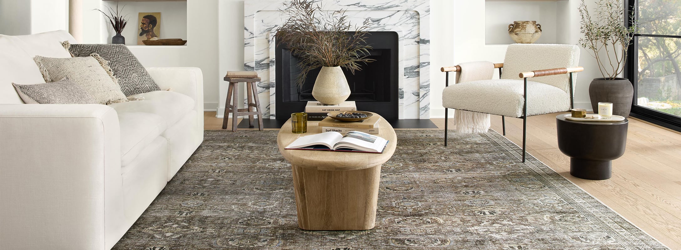 Elegant living room featuring a muted vintage-patterned rug, complementing natural wood tones, cozy seating, and a marble fireplace