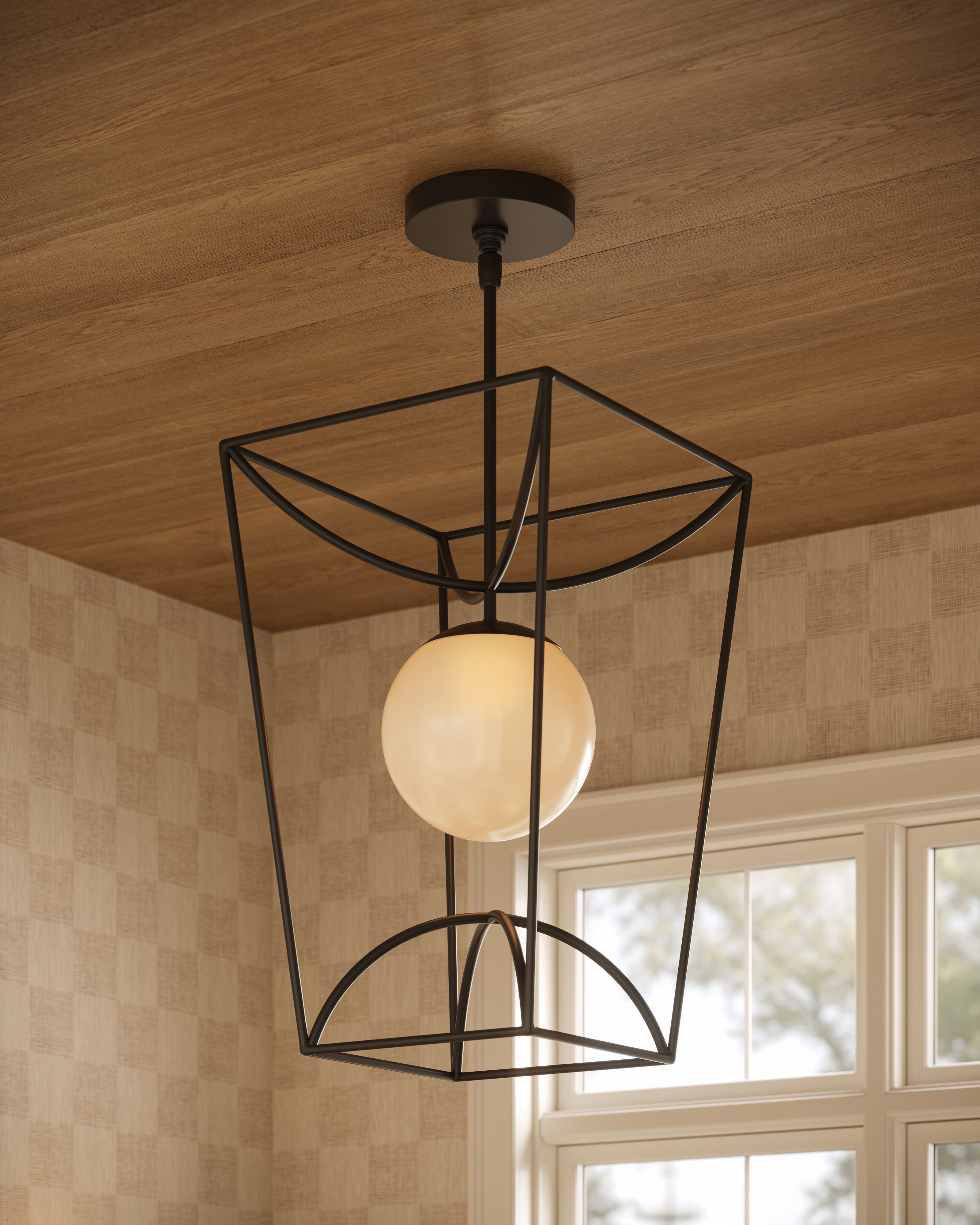 Lantern pendant light with an open black tapering metal frame and milky glass globe, hanging from a wood ceiling in a room with beige checkerboard wallpaper and white-trimmed windows.