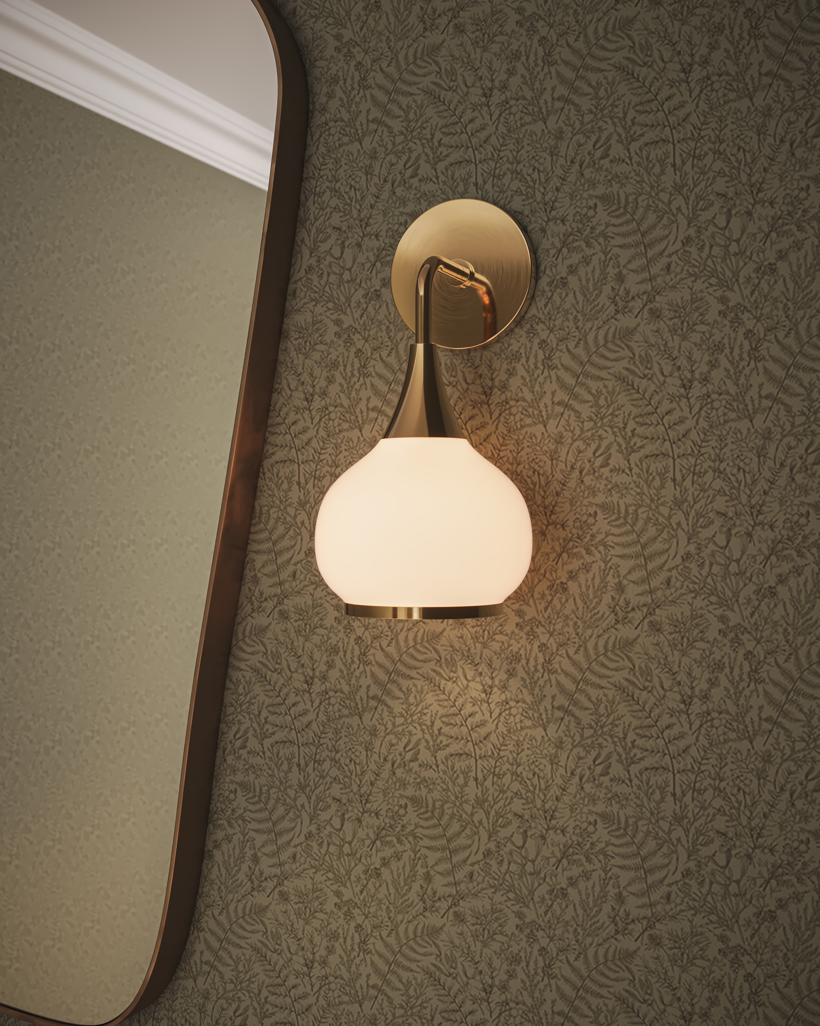 Aged gold wall sconce with opal glass shade mounted on a patterned wallpapered wall beside a curved mirror.