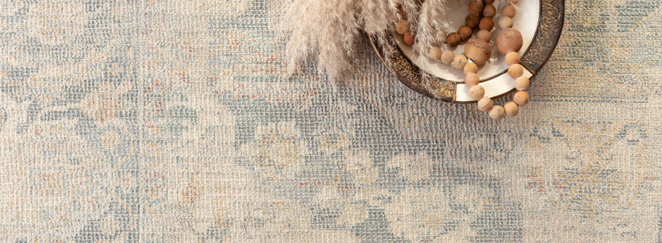 Delicate cotton blend area rug with faded floral patterns in soft blue and beige tones, styled with rustic decor for a vintage charm.