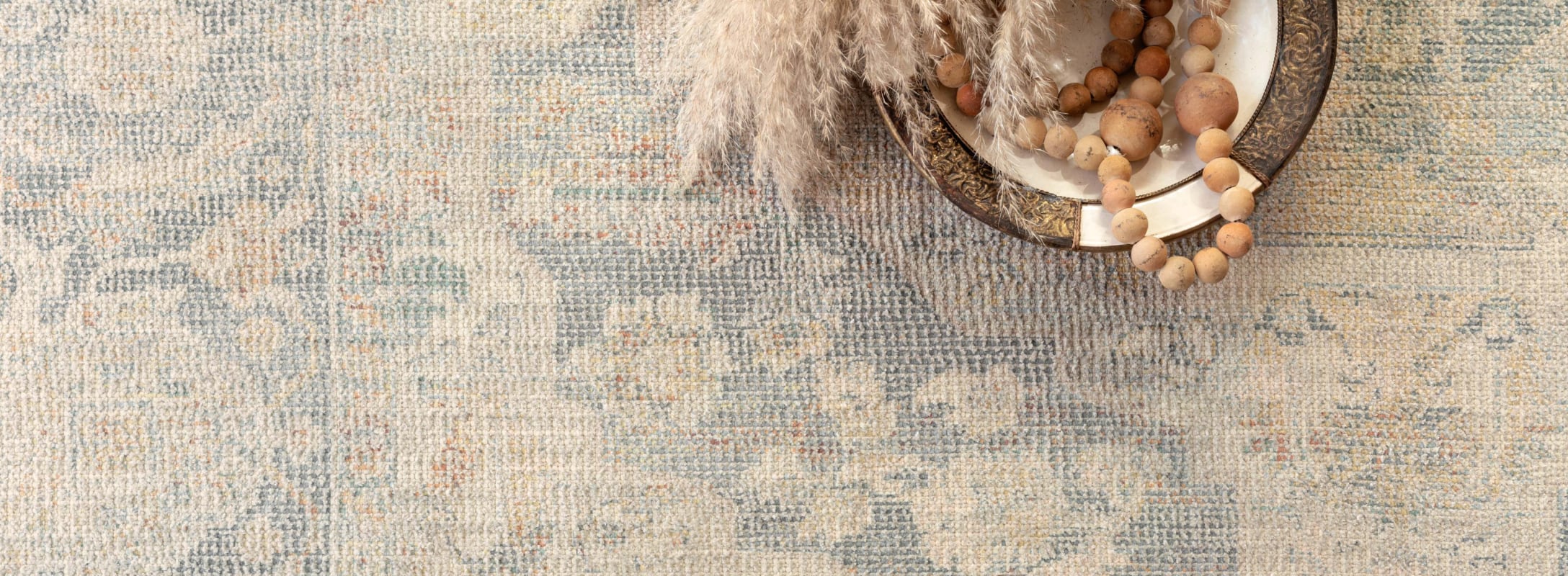 Close-up of a textured rug in warm, muted tones with intricate patterns, paired with a decorative bowl and natural accents.