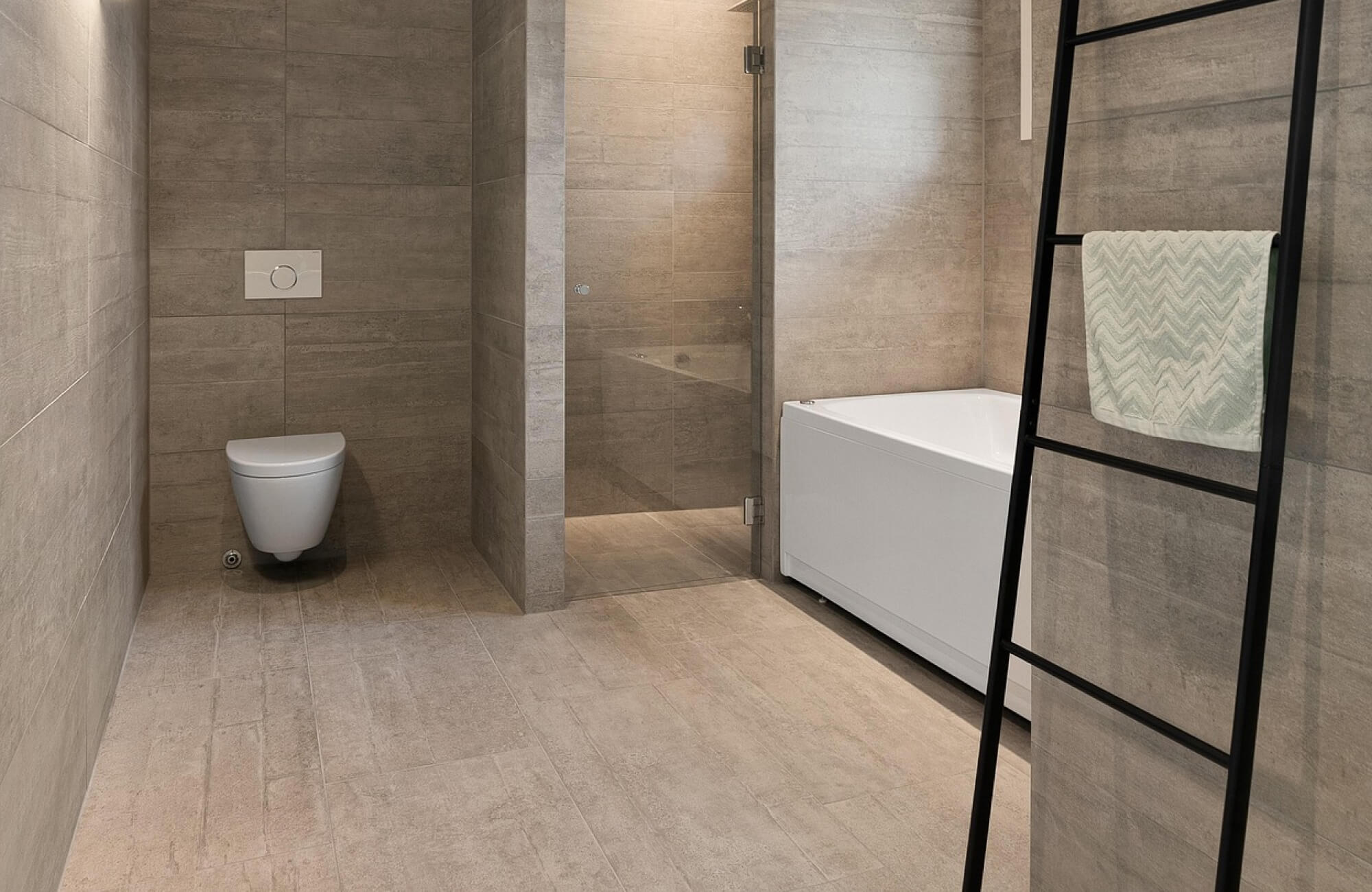 Contemporary bathroom showcasing neutral-toned bathroom tile with a stone-like texture, seamlessly covering the walls and floor to create a cohesive, minimalist look complemented by a glass shower and sleek fixtures.