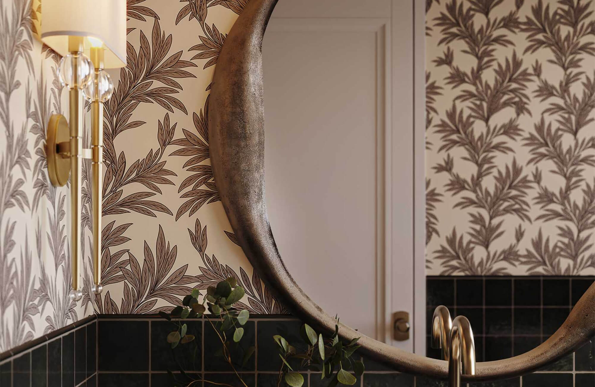 Luxury bathroom with botanical wallpaper mural, round bronze mirror, brass wall sconce, and black tile wainscoting creating layered depth.