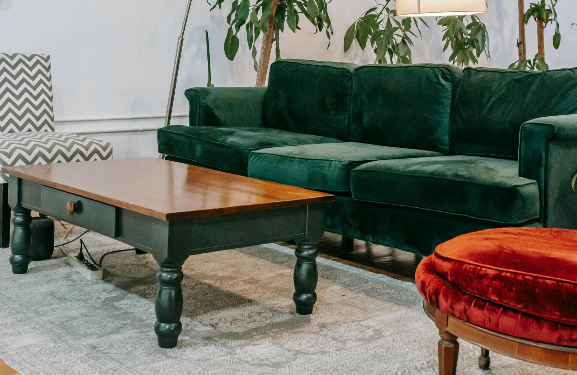 Inviting living room showcasing a 5x7 patterned rug beneath a dark wood coffee table, complemented by a deep green velvet sofa and warm ambient lighting from a floor and table lamp.