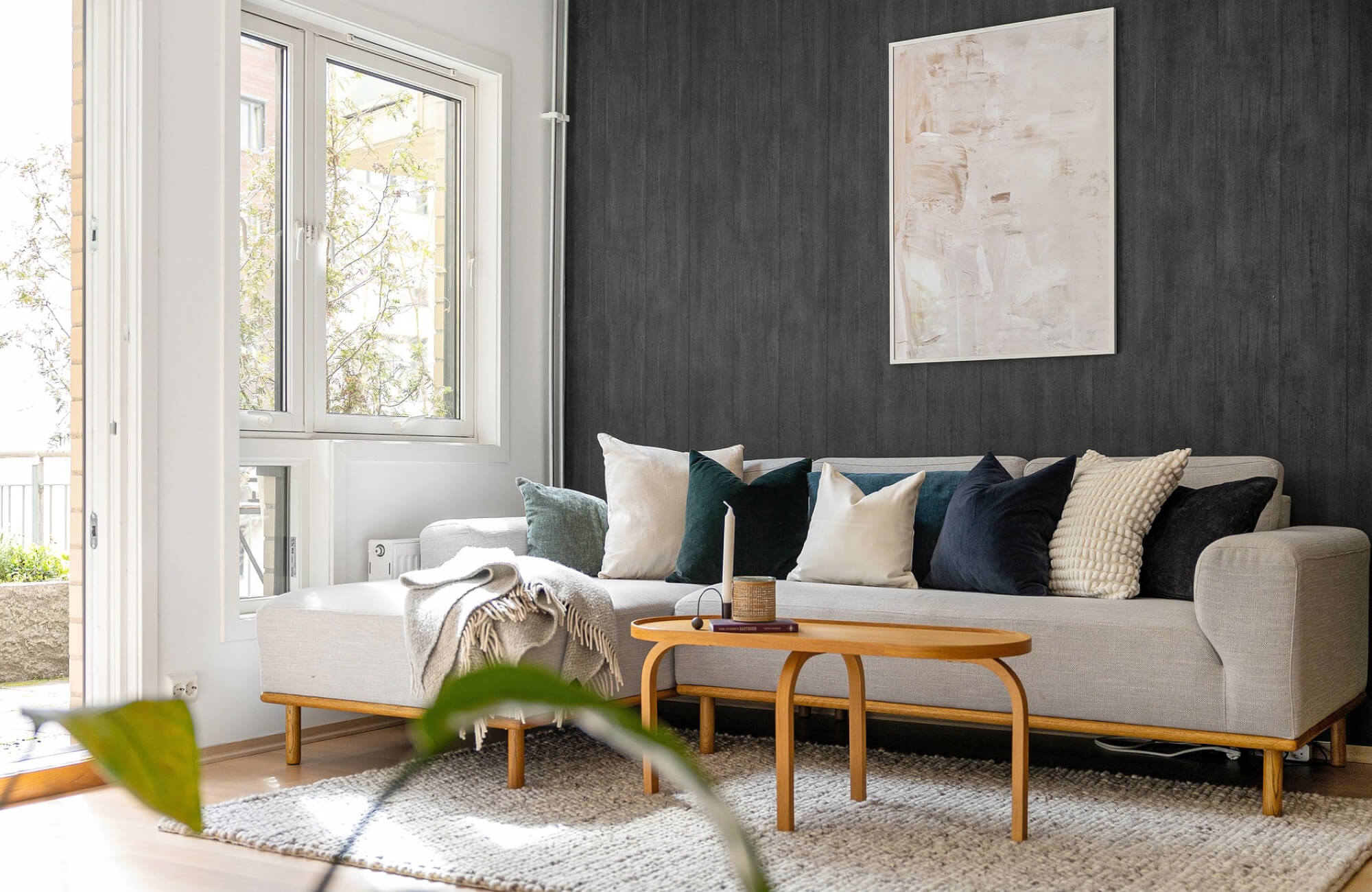Decorative pillow arrangement on a light gray sectional sofa, featuring cream, deep green, and navy cushions styled against a dark accent wall in a modern living room.