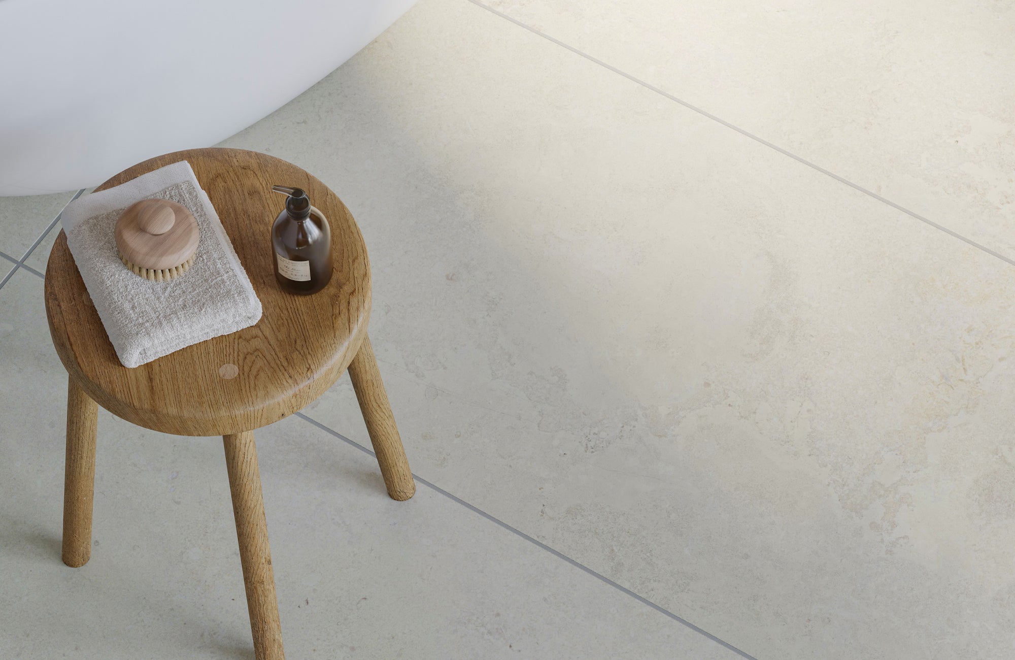 Large-format bathroom tile flooring shown beneath a wooden stool, highlighting minimal grout lines and subtle texture.