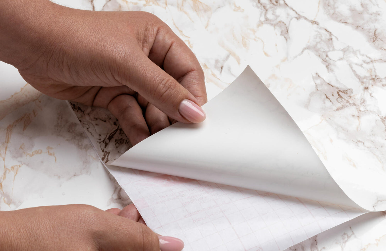 Hand peeling backing from marble-pattern peel and stick wallpaper before installation on a smooth surface.
