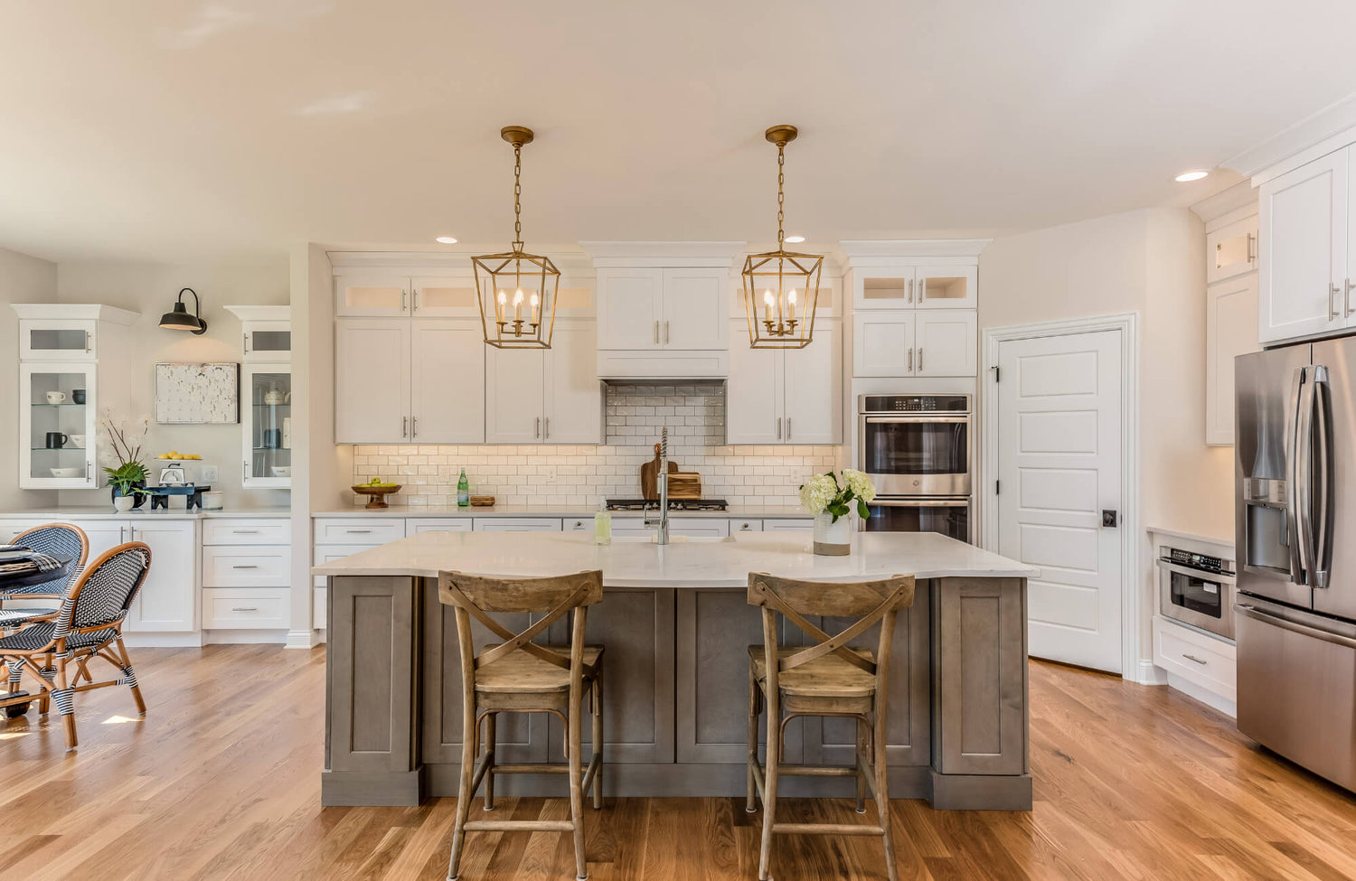 Modern kitchen with white cabinetry, a gray island, brass pendant lights, wood flooring, and two rustic wood bar stools.
