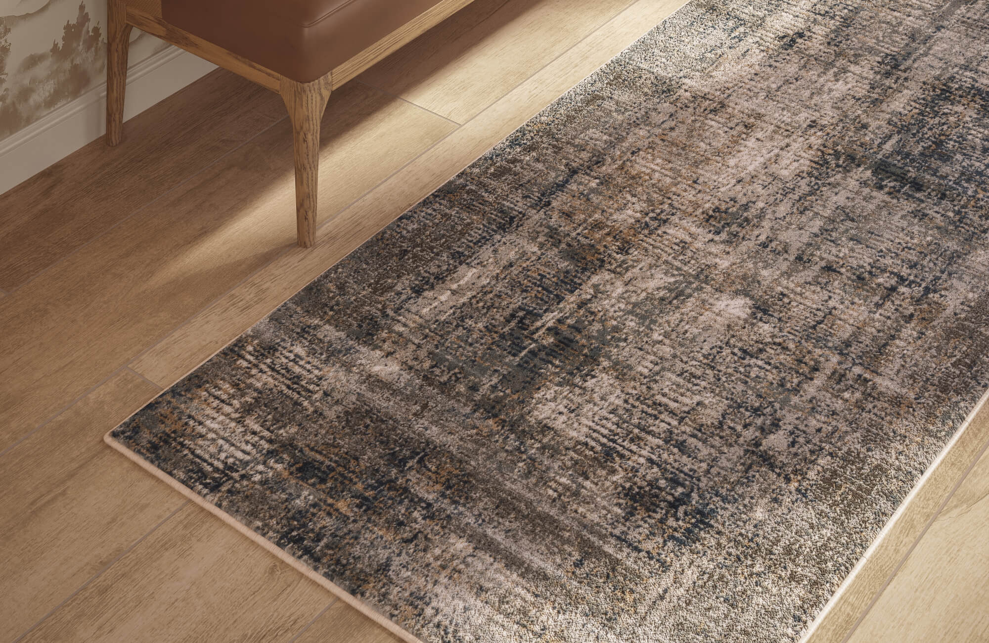 Distressed bone and slate area rug layered over warm wood flooring, adding soft texture beside a brown leather chair.