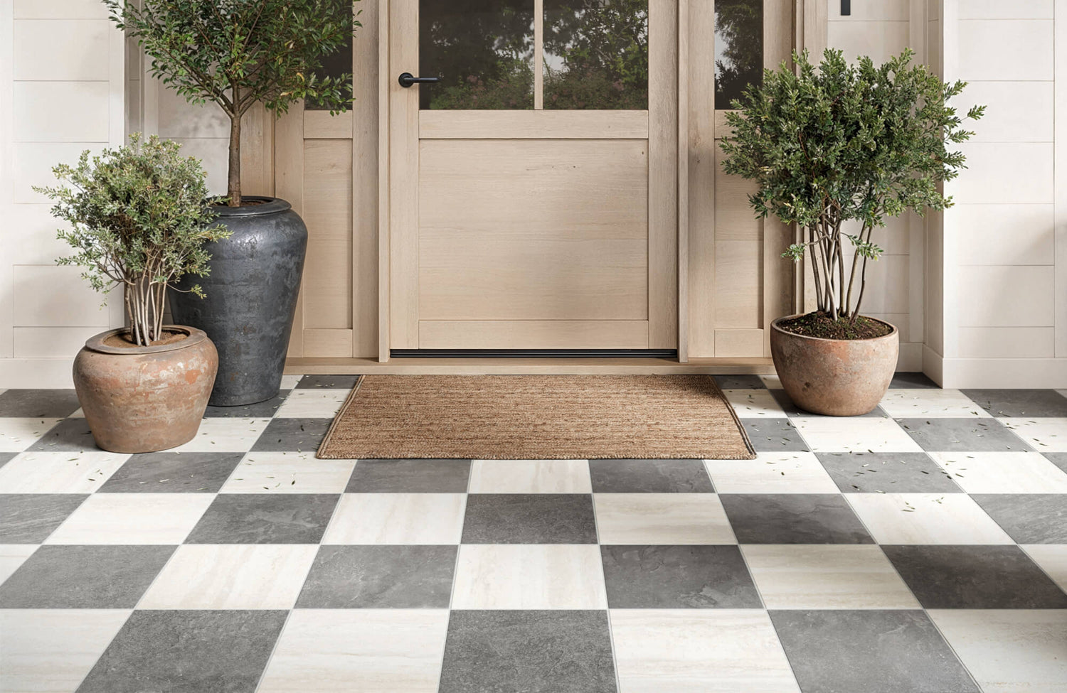 Checkerboard entryway with large format gray and white pavers, terracotta planters, and a light wood door with glass panels.