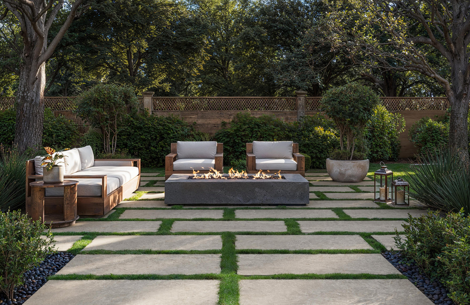 Modern outdoor patio with large beige porcelain pavers set in grass, surrounding a sleek concrete fire pit and wooden lounge seating.