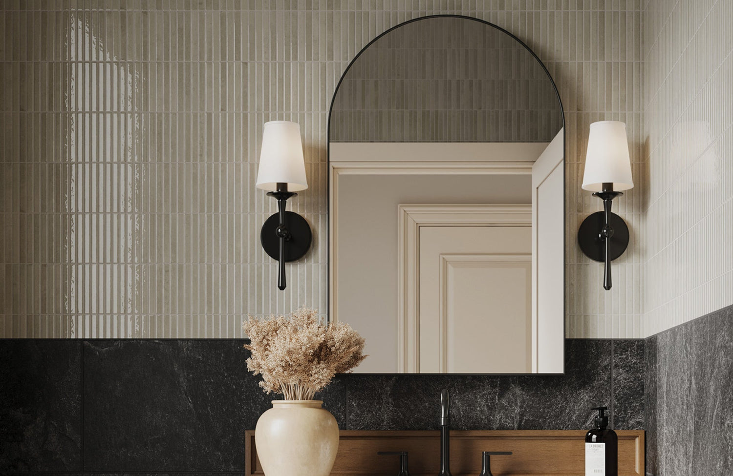 Elegant black wall sconces with white shades add symmetry and warmth to a modern bathroom vanity with tiled walls.