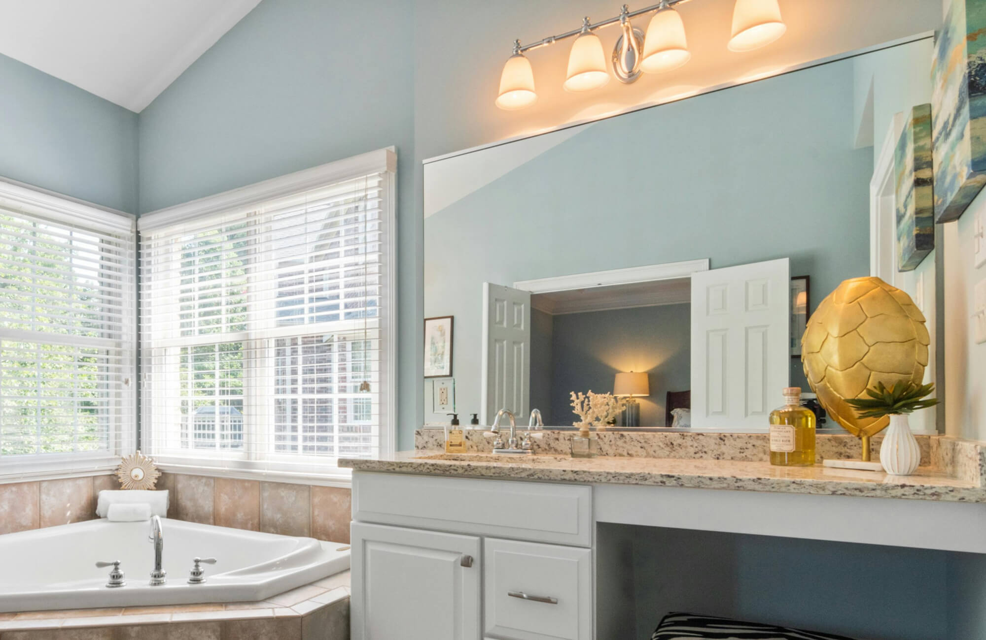 Bright bathroom vanity lighting with four frosted glass sconces in a polished chrome fixture, illuminating a granite countertop and large wall mirror for a refined, modern appeal.