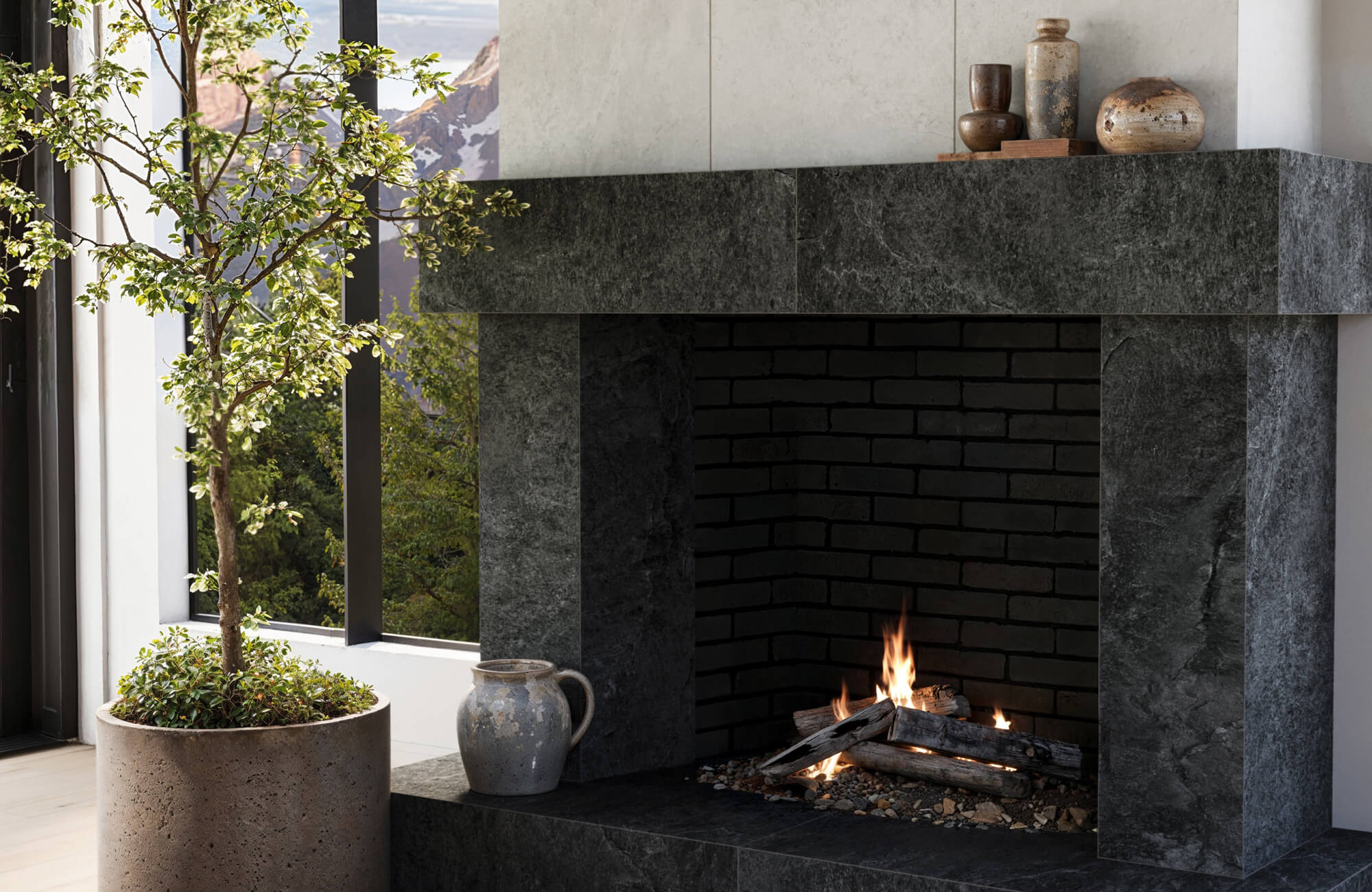Decorative vase accents with weathered ceramic finishes styled on a dark stone fireplace mantel create layered texture and organic modern character in a contemporary living space.