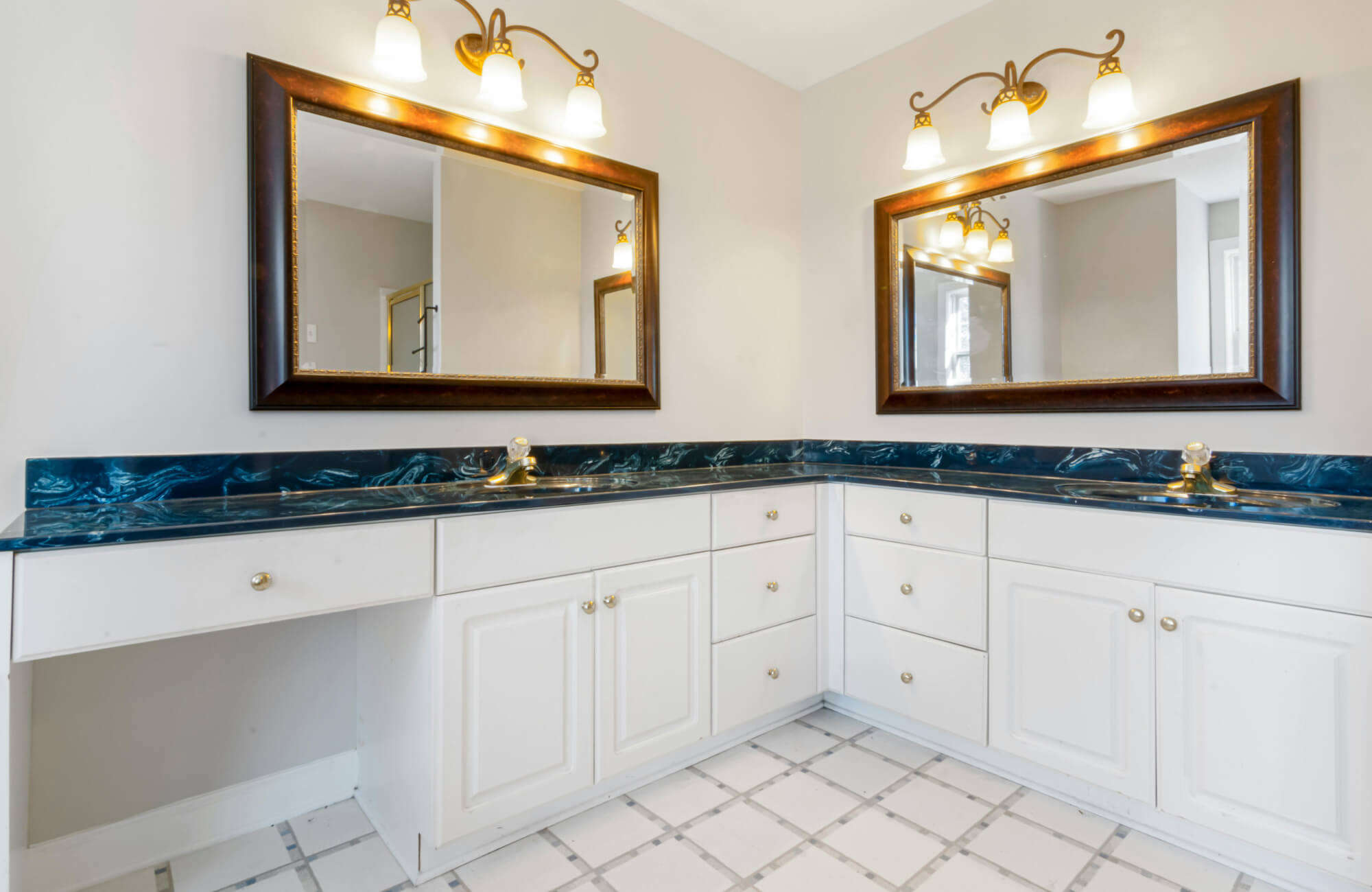 Traditional corner vanity bathroom with dark wood-framed mirrors, elegant brass light fixtures, and glossy blue marble countertops.