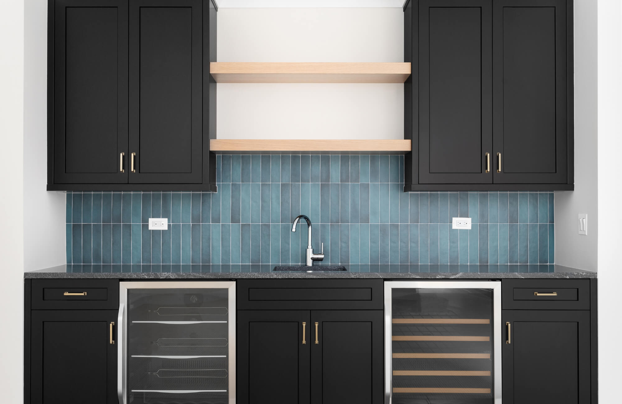 Bar area with matte black cabinetry, open wood shelves, and a vertical blue ceramic tile backsplash behind a stainless steel faucet.