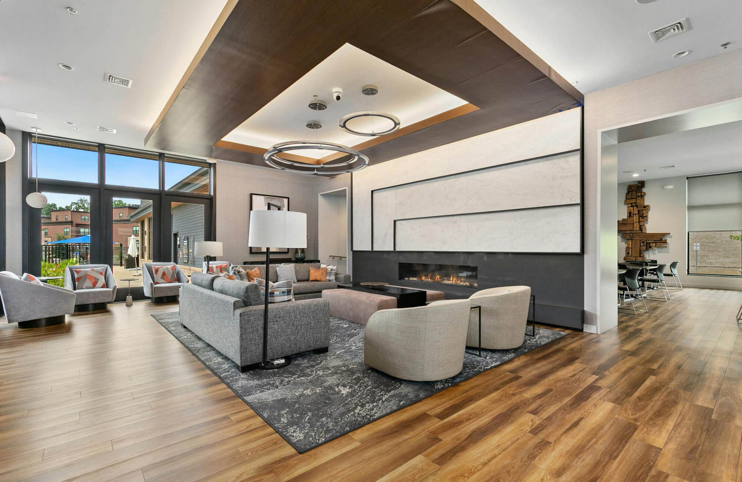 Modern living room with wood-look porcelain tile flooring, gray seating, and a sleek fireplace under warm, recessed ceiling lights.