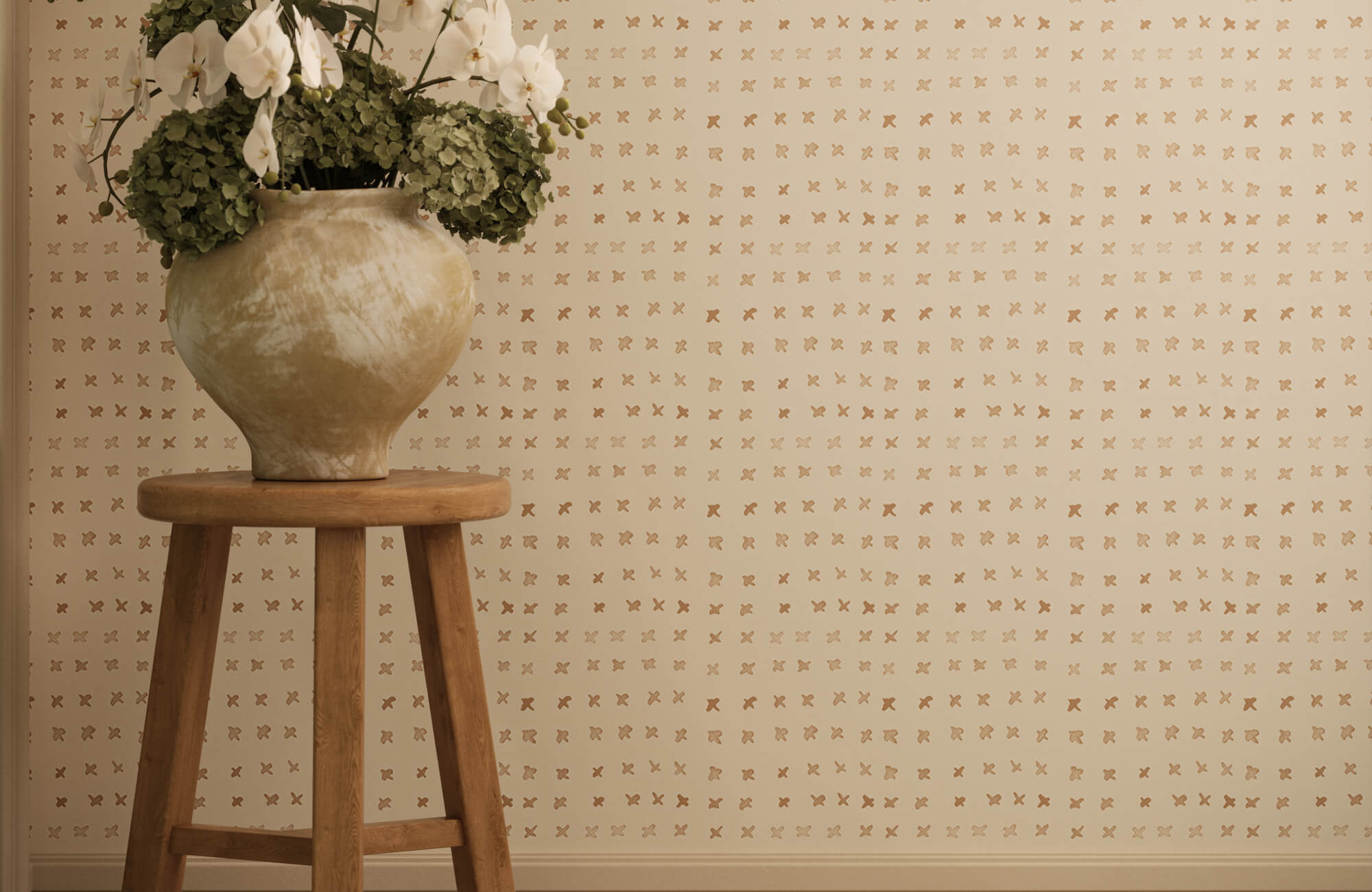 Elegant cream wallpaper with metallic cross motifs beside a wooden stool topped with white orchid arrangements.