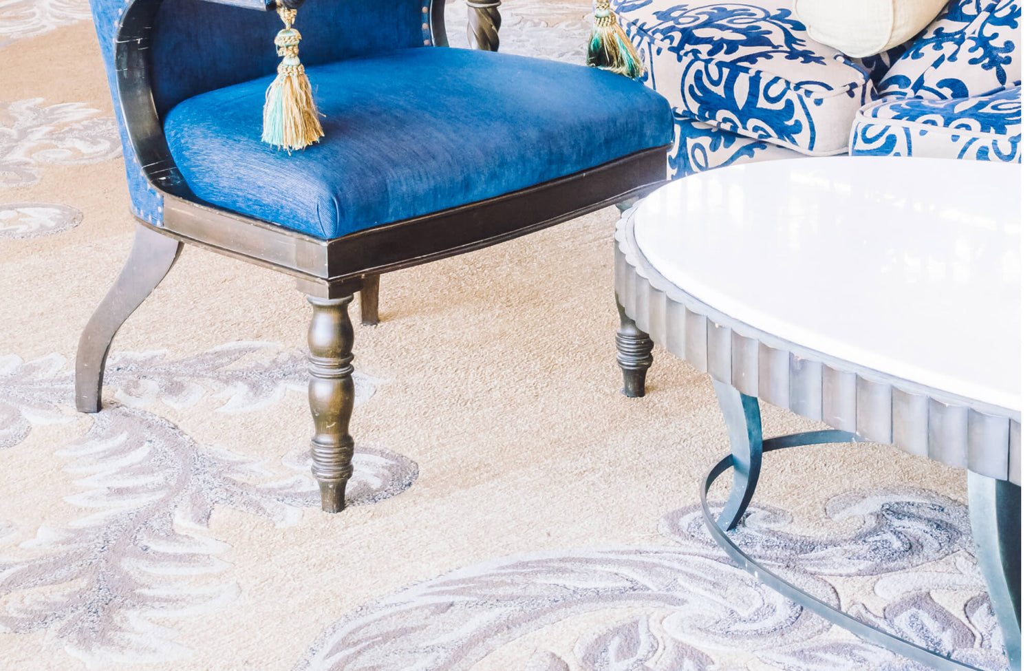A cool rug with soft beige and gray swirling motifs grounds the seating area, subtly complementing the rich blue upholstered chair and patterned sofa while adding an airy, refined elegance to the space.