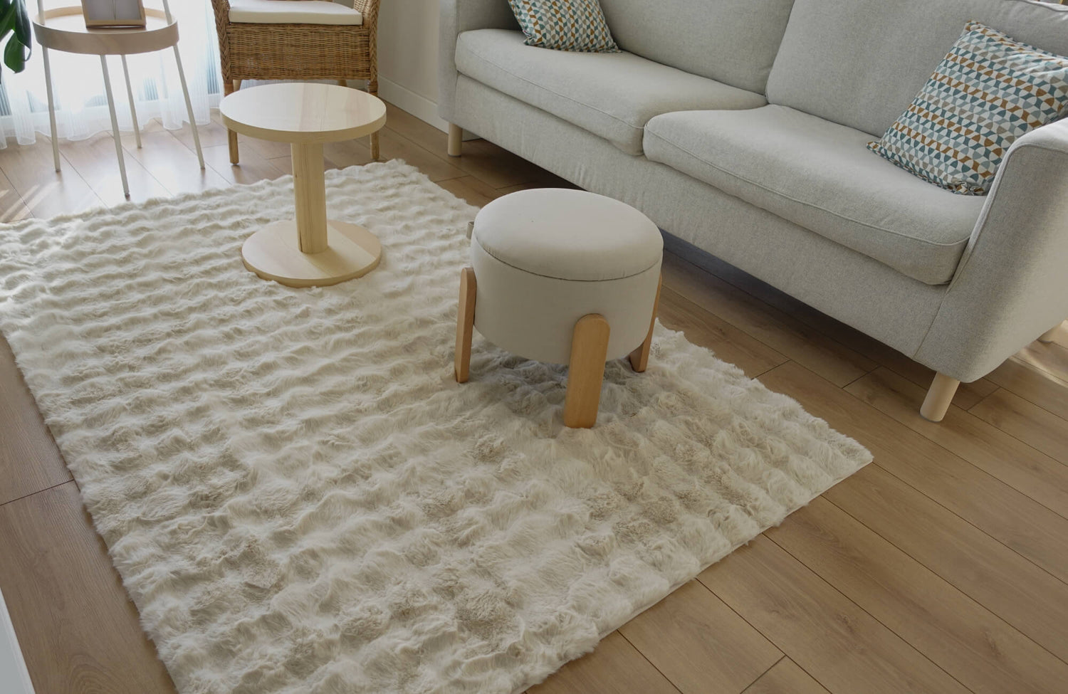 A soft cream wool rug in a bright living room with light-wood furniture, a gray sofa, and natural textures creating a cozy, airy space.