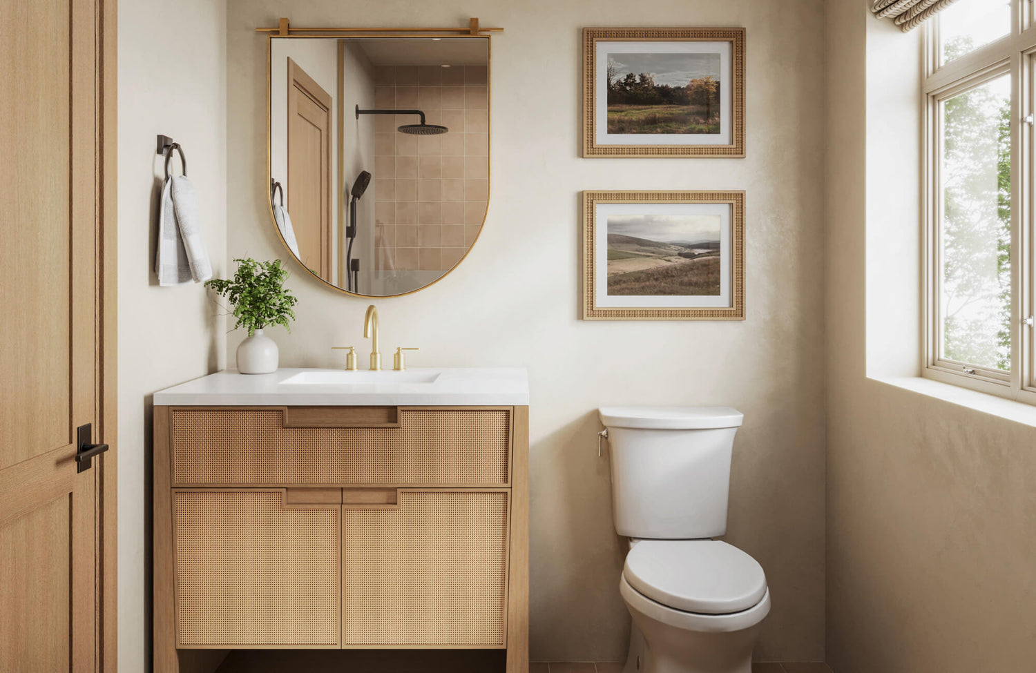 Modern bathroom with a round brass-framed mirror, rattan vanity, gold fixtures, and neutral wall art beside a window with natural light.