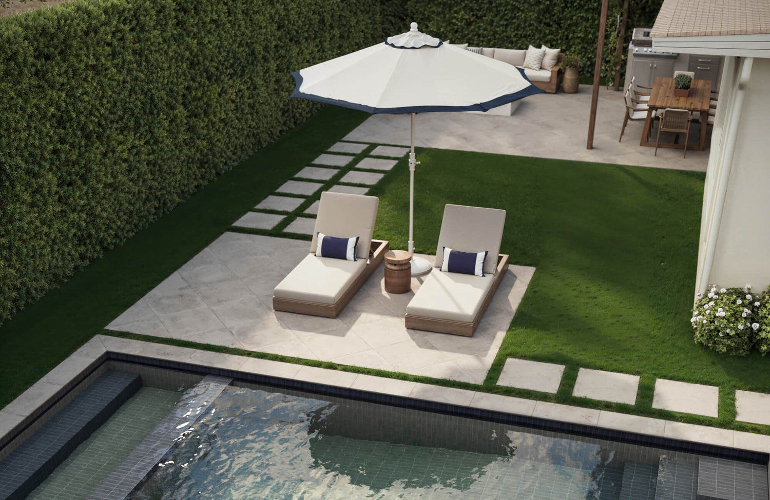 Light porcelain pavers surround a modern poolside setup with lounge chairs, umbrella shade, and lush green grass.