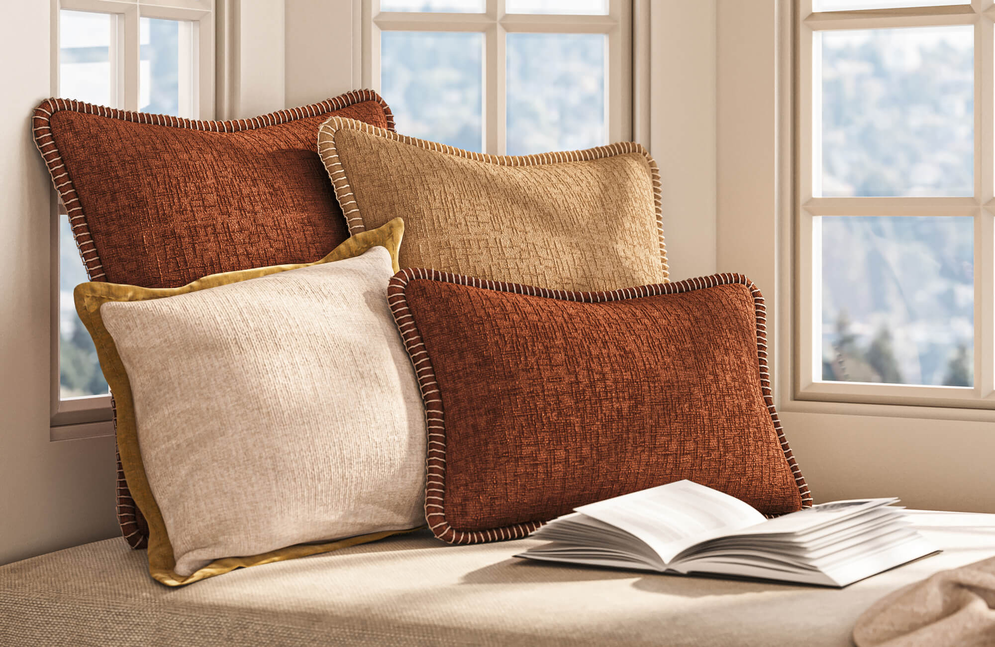 Terracotta, tan, and off-white decorative pillows with stitched edges on a window seat beside an open book.