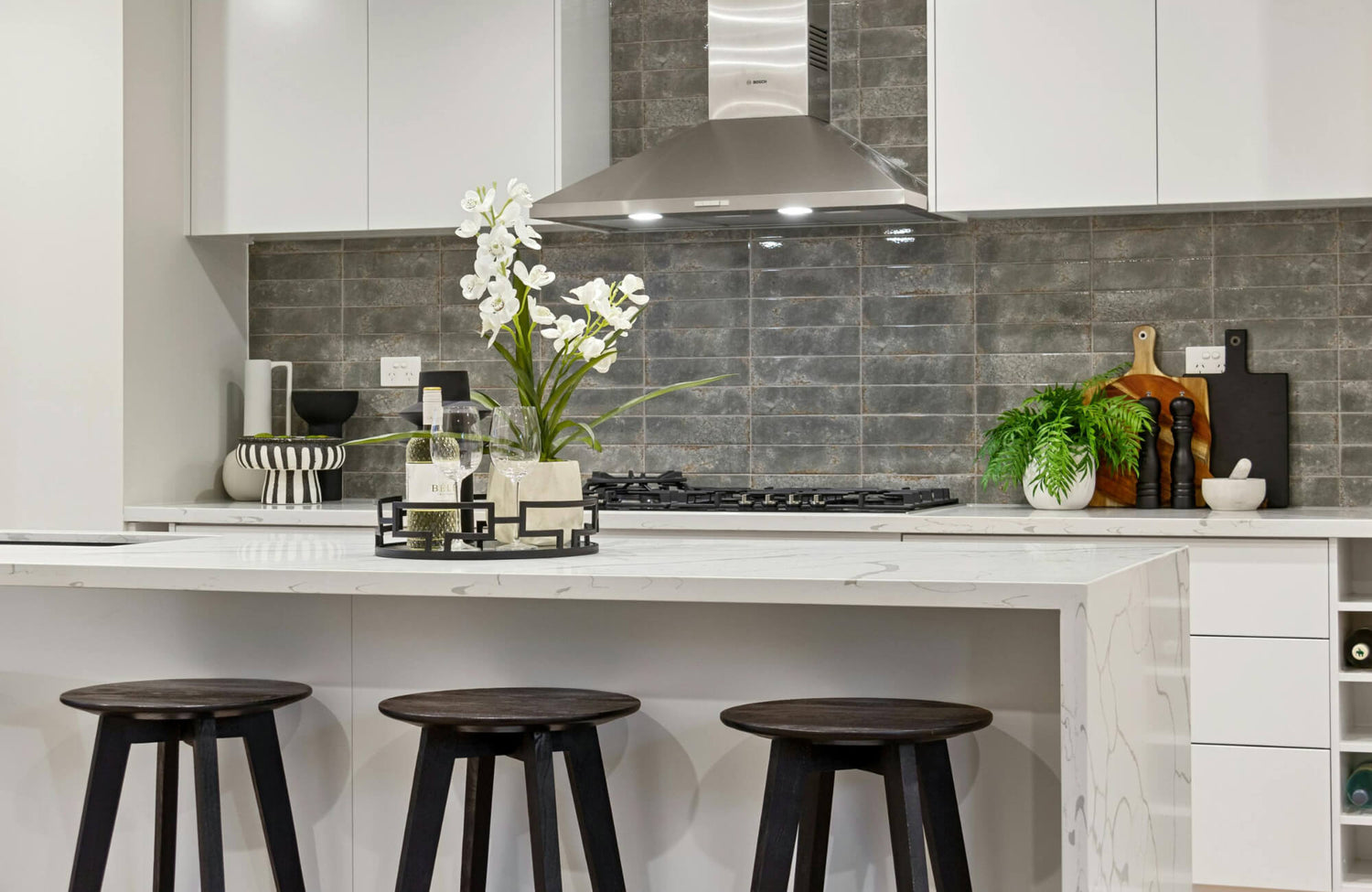 Modern kitchen with gray zellige-style tile backsplash, white cabinetry, and stainless steel range hood highlighting subtle grout lines.