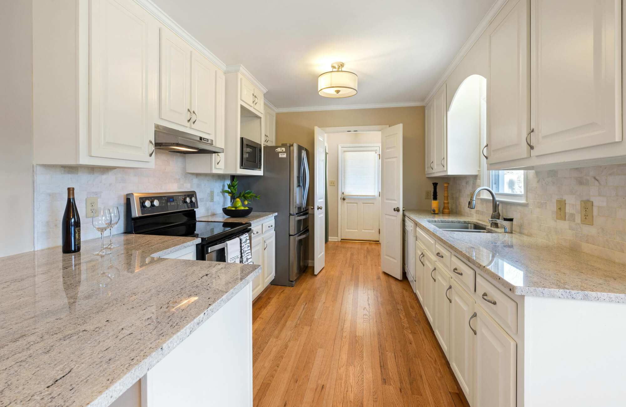 Bright galley kitchen with white cabinets, granite counters, and a simple ceiling light illuminating the narrow layout.