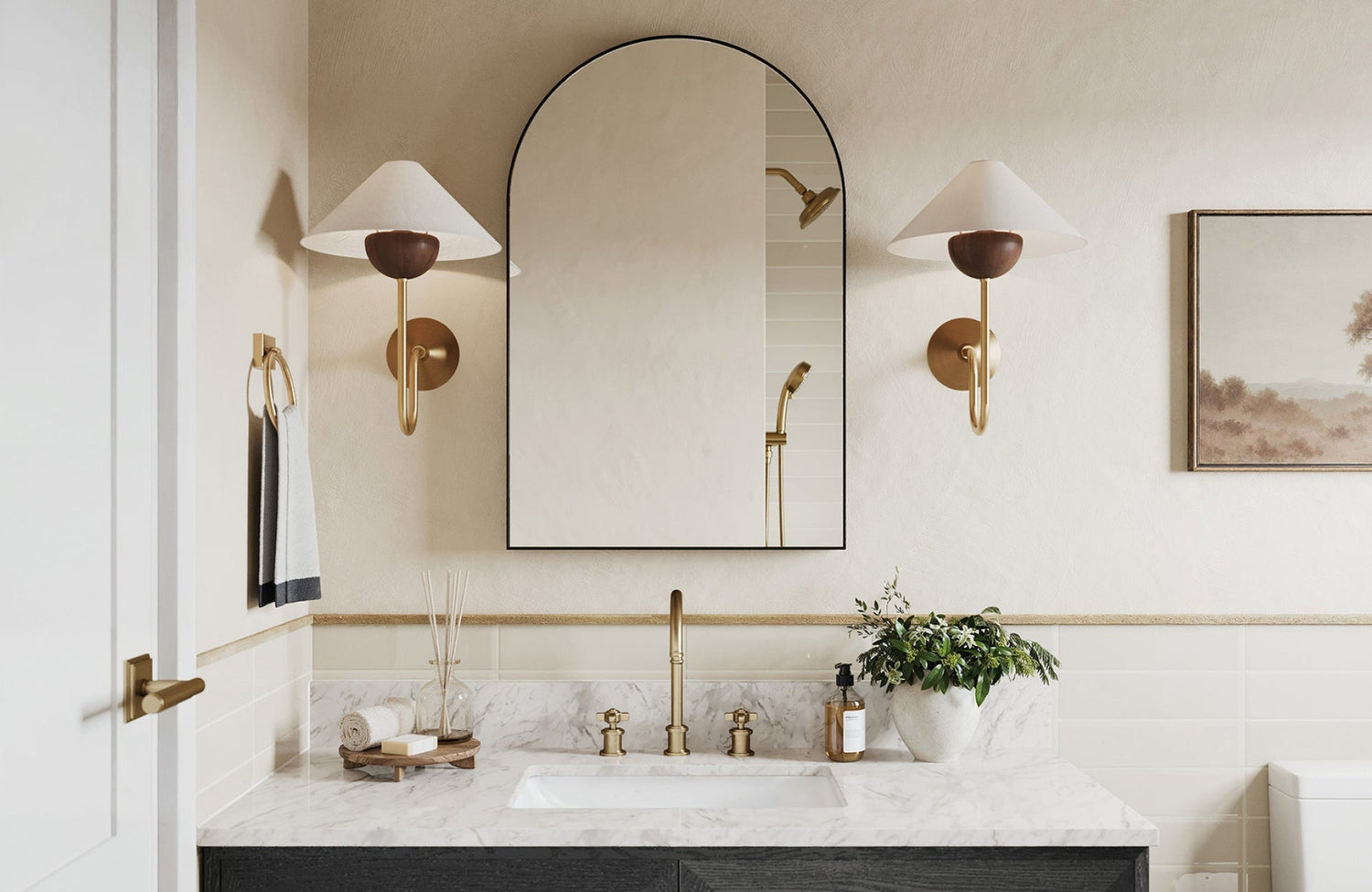 Arched black-framed mirror above a single-sink vanity with marble top, framed by warm brass wall sconces.