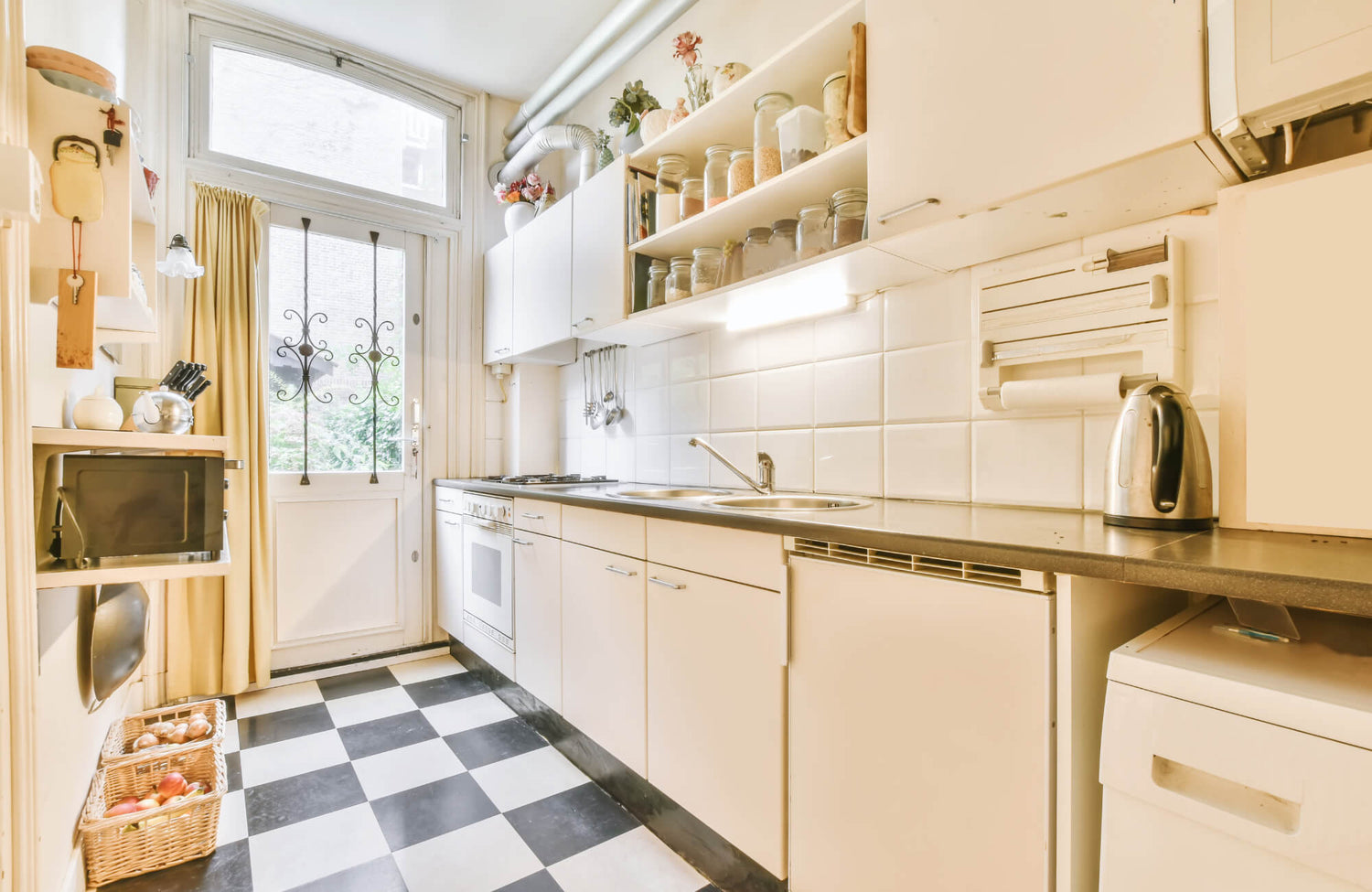 Bright kitchen with black and white checkered tile floor, cream cabinets, and warm natural light from a glass back door.