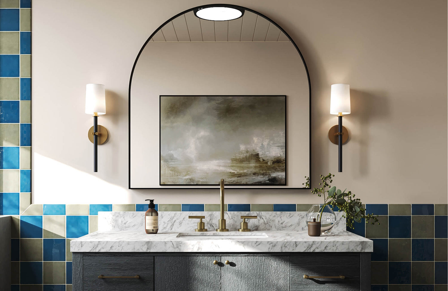 Rich blue and olive green tiles accent a modern vanity with a marble top, brass fixtures, and a striking arched mirror.