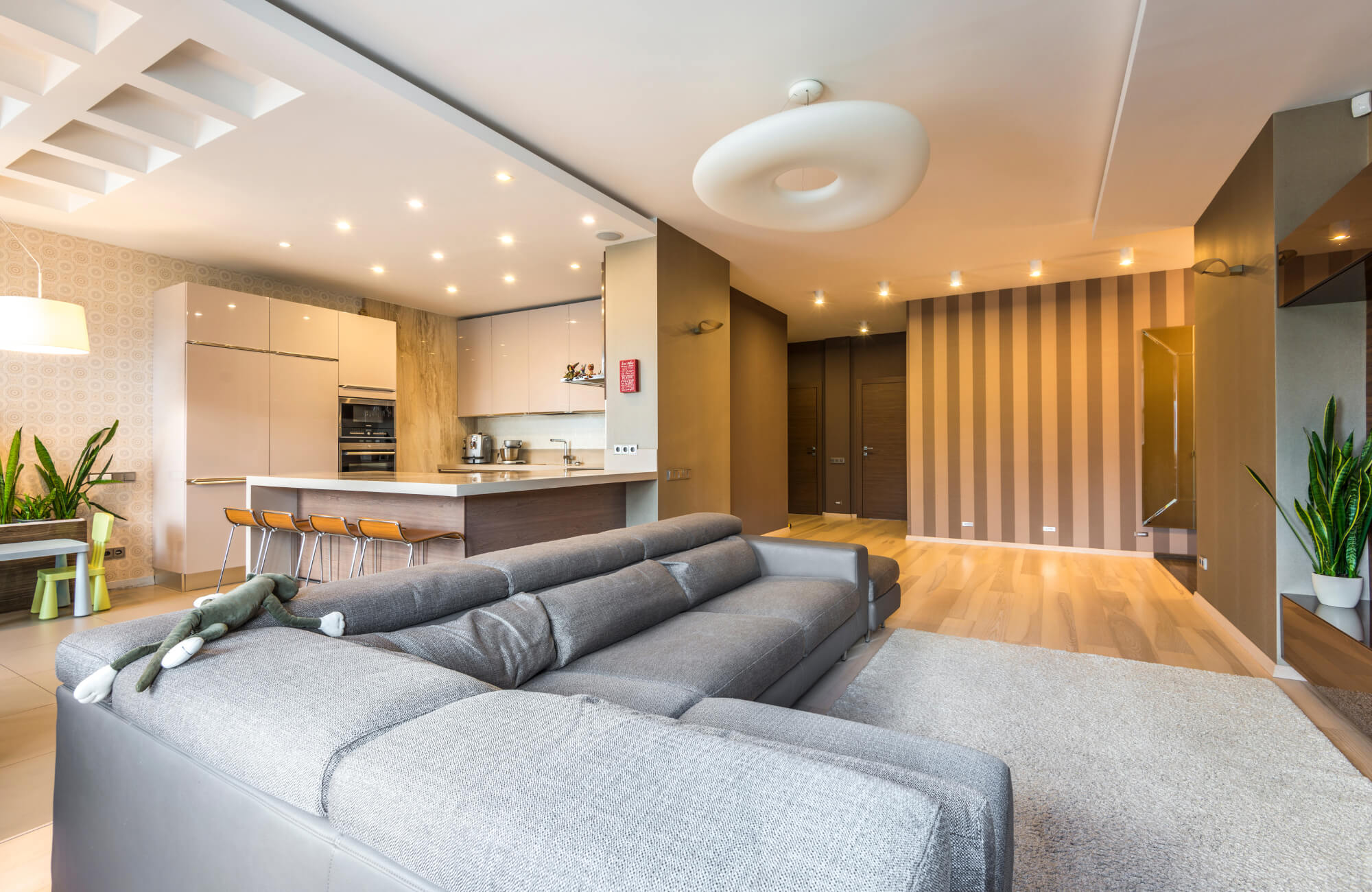 Modern open-plan living room with grey sectional sofa, stylish kitchen island, and contemporary flush mount ceiling light.