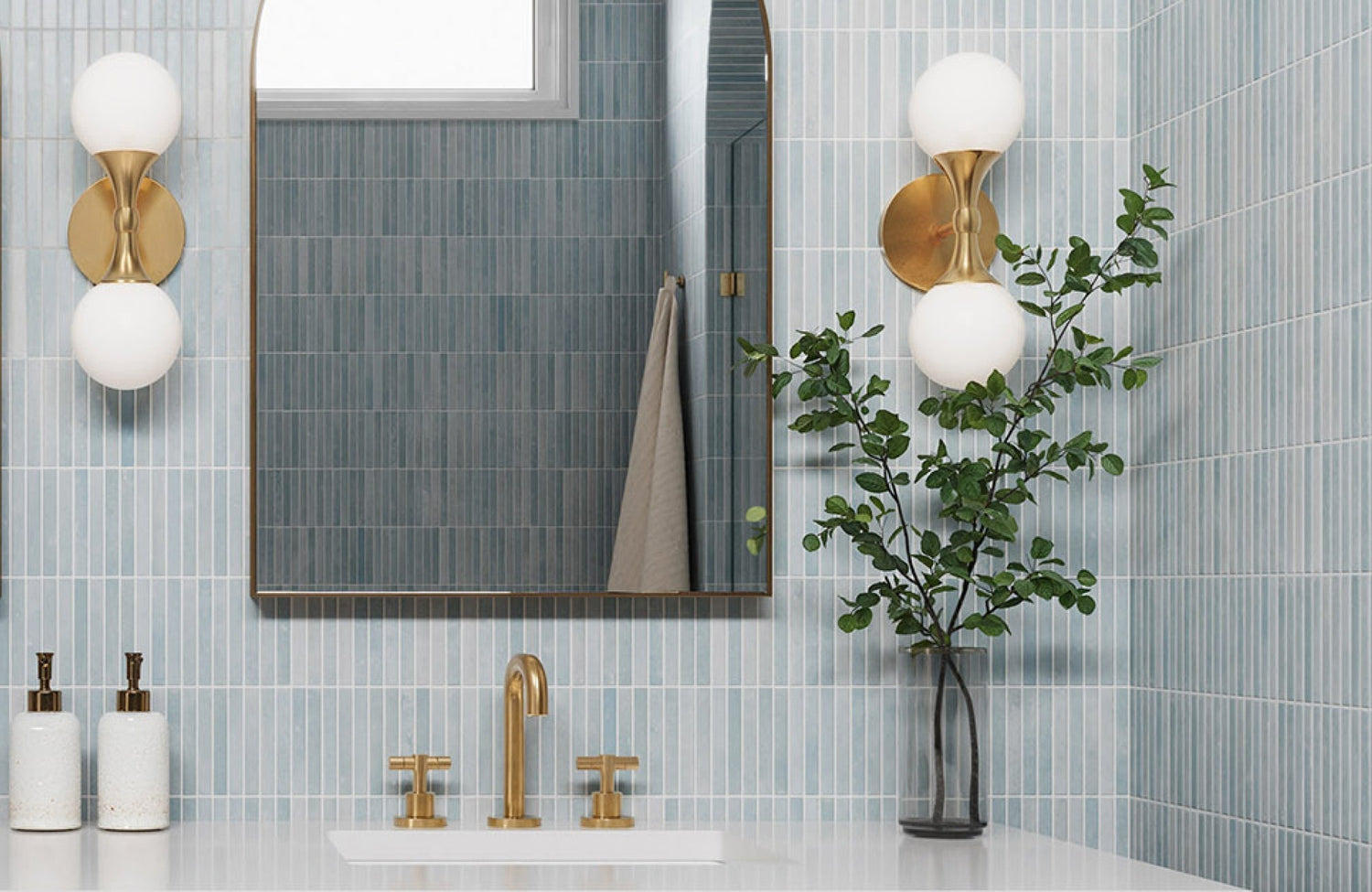 Brass double globe wall sconces in a blue-tiled bathroom with modern brass fixtures and a rectangular mirror