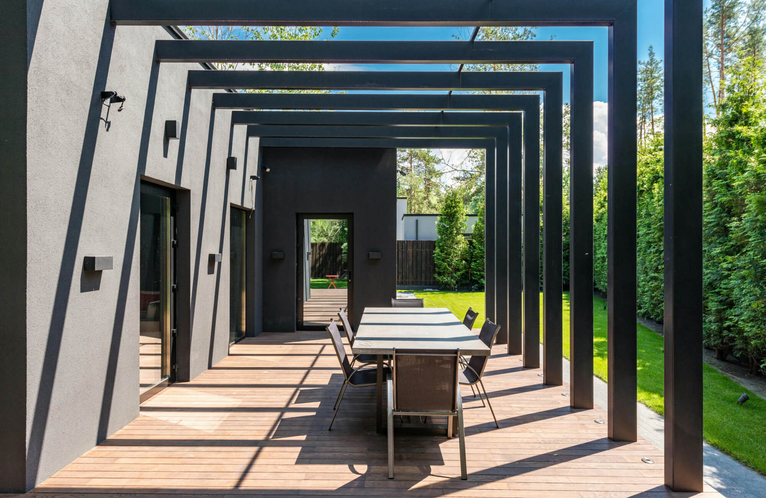 Outdoor dining setup framed by clean-lined pergola beams, pairing sleek chairs with warm decking for a contemporary backyard setting.