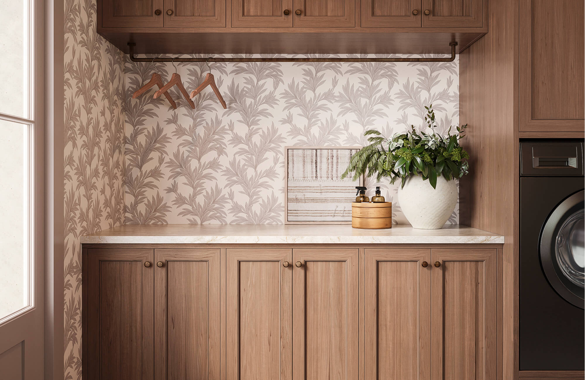 Classic laundry room with warm wood cabinetry, leafy wallpaper, wall art, stone countertop, and integrated hanging rod detail.