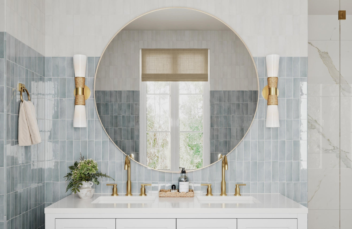 Elegant bathroom with vertical blue zellige tiles, oversized round mirror, gold double faucets, and white-and-gold bowtie sconces.