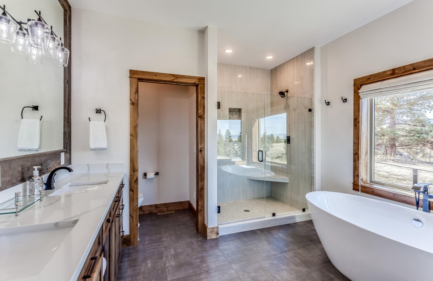 Modern bathroom with glass-enclosed shower, freestanding tub, wood trim accents, and double vanity with white countertops.