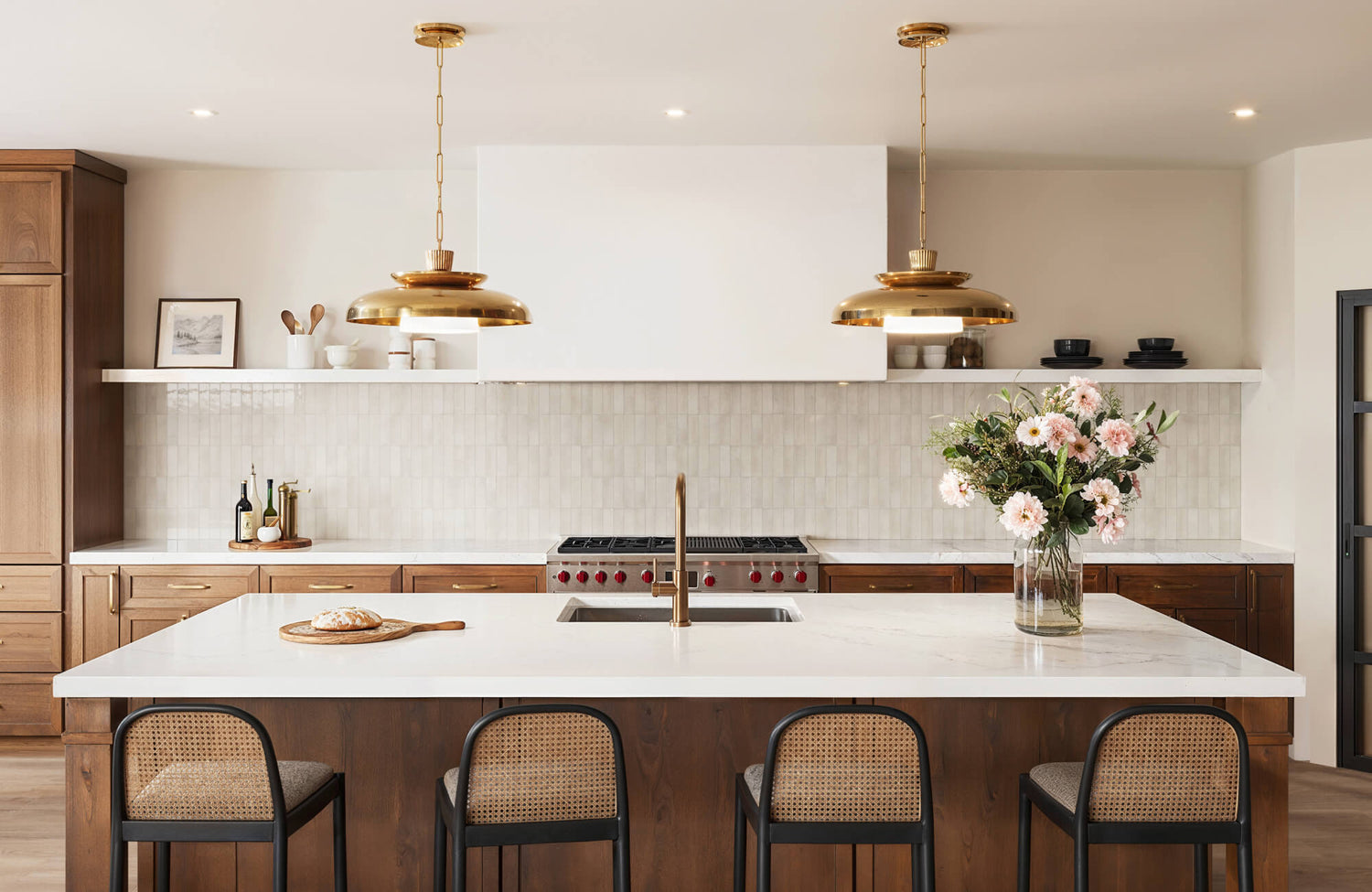 Cream subway tile backsplash in a modern kitchen with white countertops, warm wood cabinetry, brass pendant lights, and woven bar stools.