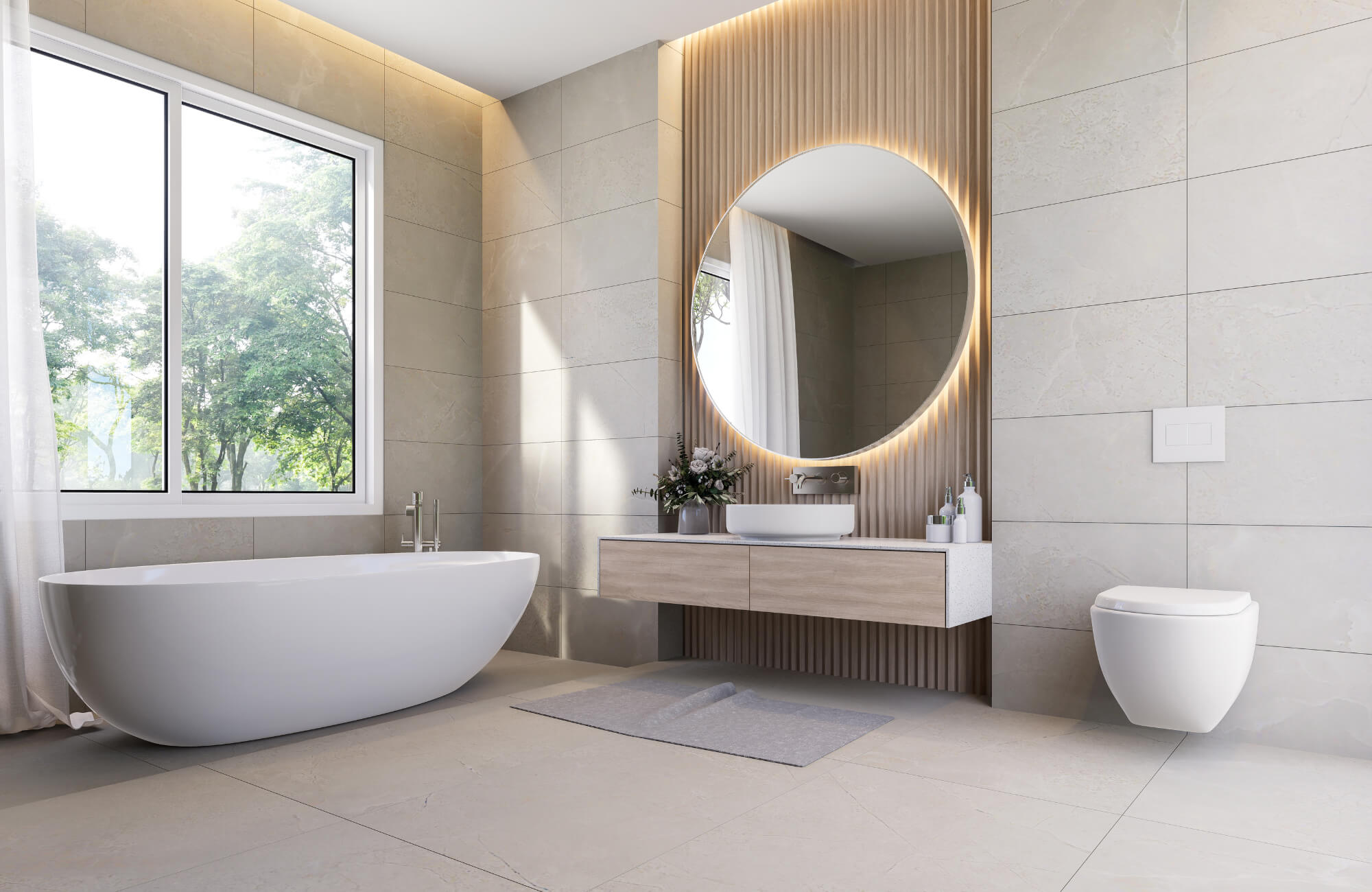 Modern bathroom with a large round mirror near a sunny window, showing how natural light reflects across neutral tile surfaces.