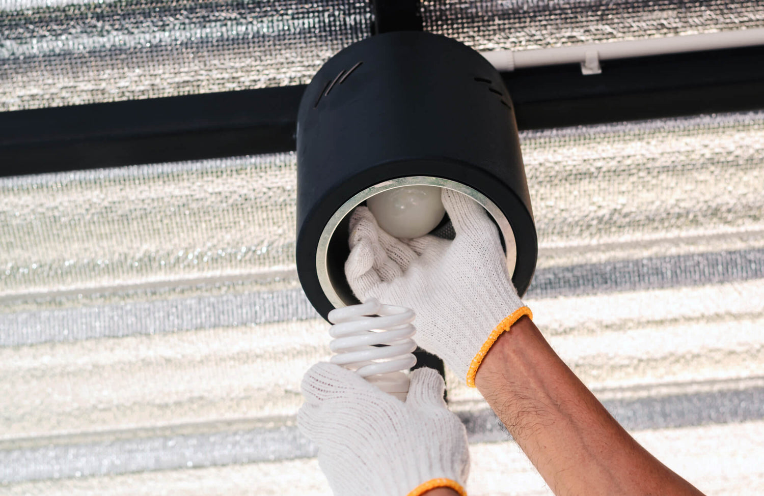 Person wearing white gloves replacing a light bulb in a black ceiling fixture, demonstrating safe home lighting maintenance.