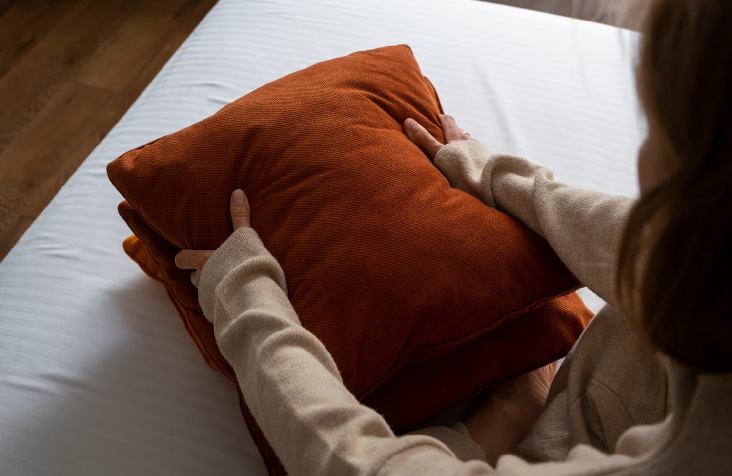 Red decorative pillow being fluffed and adjusted on a bed, showing its soft fill and everyday use.