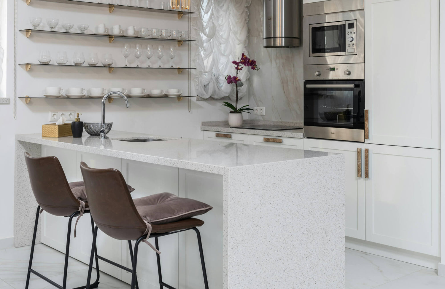 Kitchen island with stools showcased in a modern kitchen featuring a polished white waterfall-edge island, sleek leather counter stools with plush cushions, and open glass shelving.