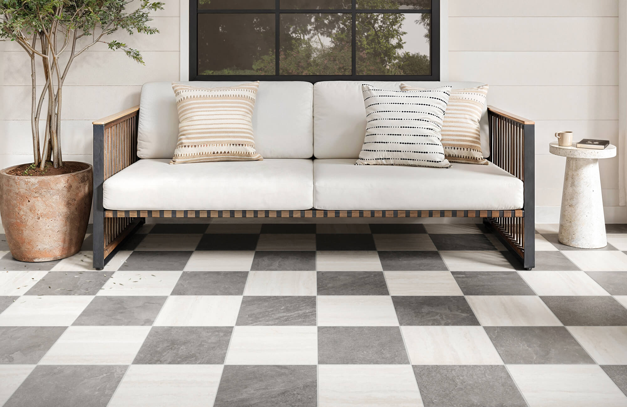 Outdoor patio with neutral checkered porcelain tile flooring styled with modern white cushioned sofa and striped throw pillows for relaxed charm