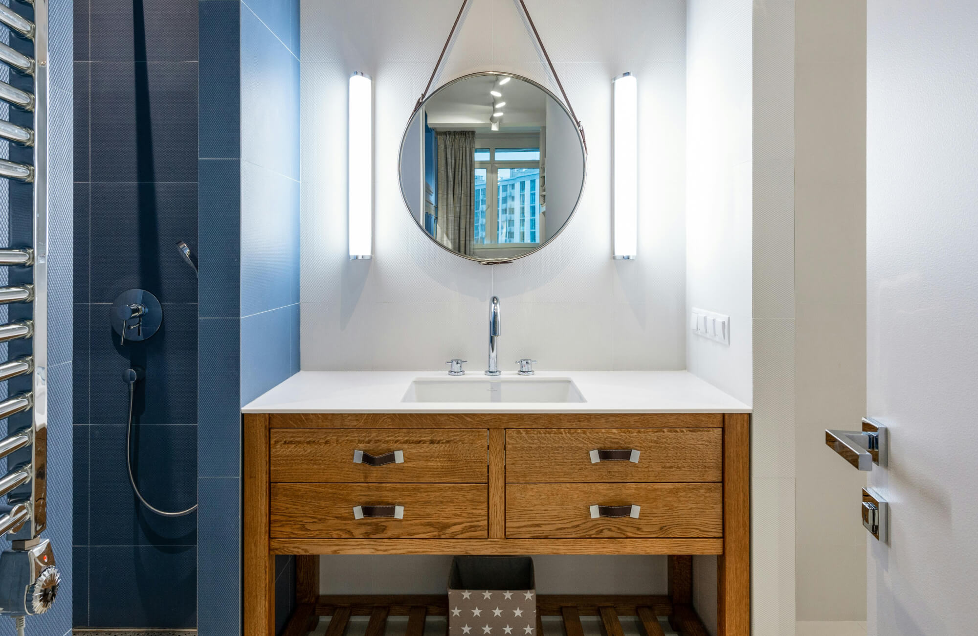 Modern bathroom vanity with a round mirror, vertical lights, and sleek blue tile shower wall.