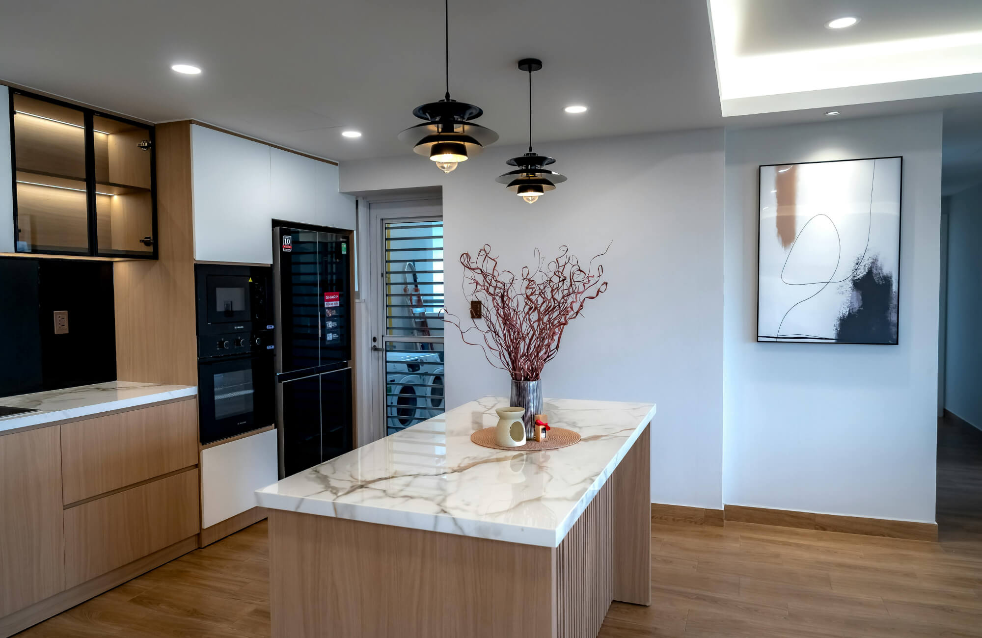 Modern kitchen with a marble island, wood cabinetry, and three black pendant lights hanging above for balanced task lighting.