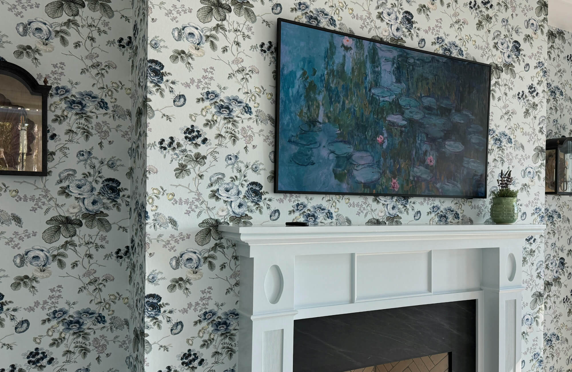 Peel and stick wallpaper with blue floral toile pattern styled behind a wall-mounted TV above a white fireplace mantel.