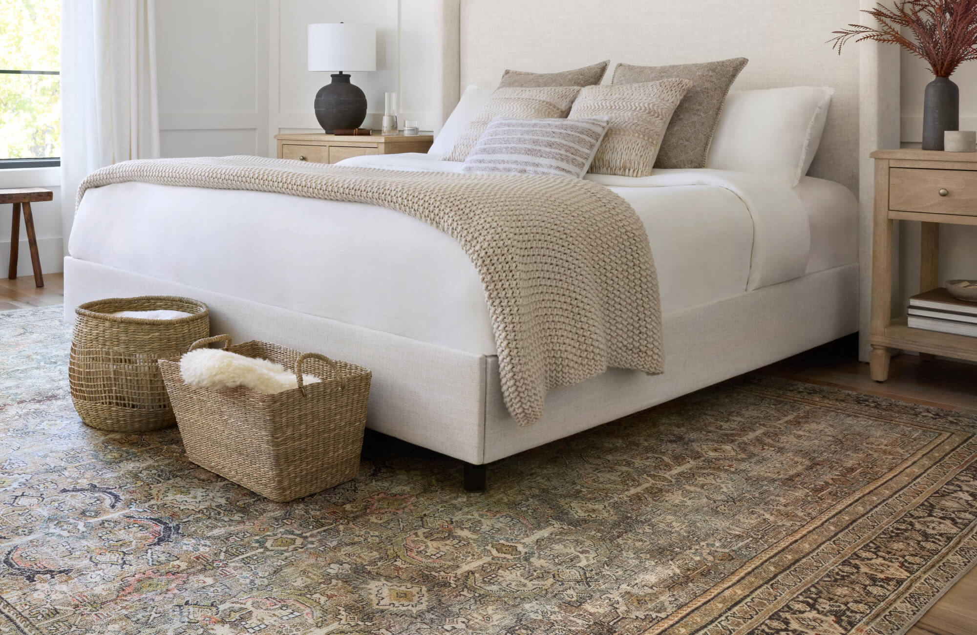 Bedroom with five decorative pillows layered on a neatly made bed, featuring two larger pillows at the back, two patterned accent pillows, and one smaller lumbar pillow at the front.