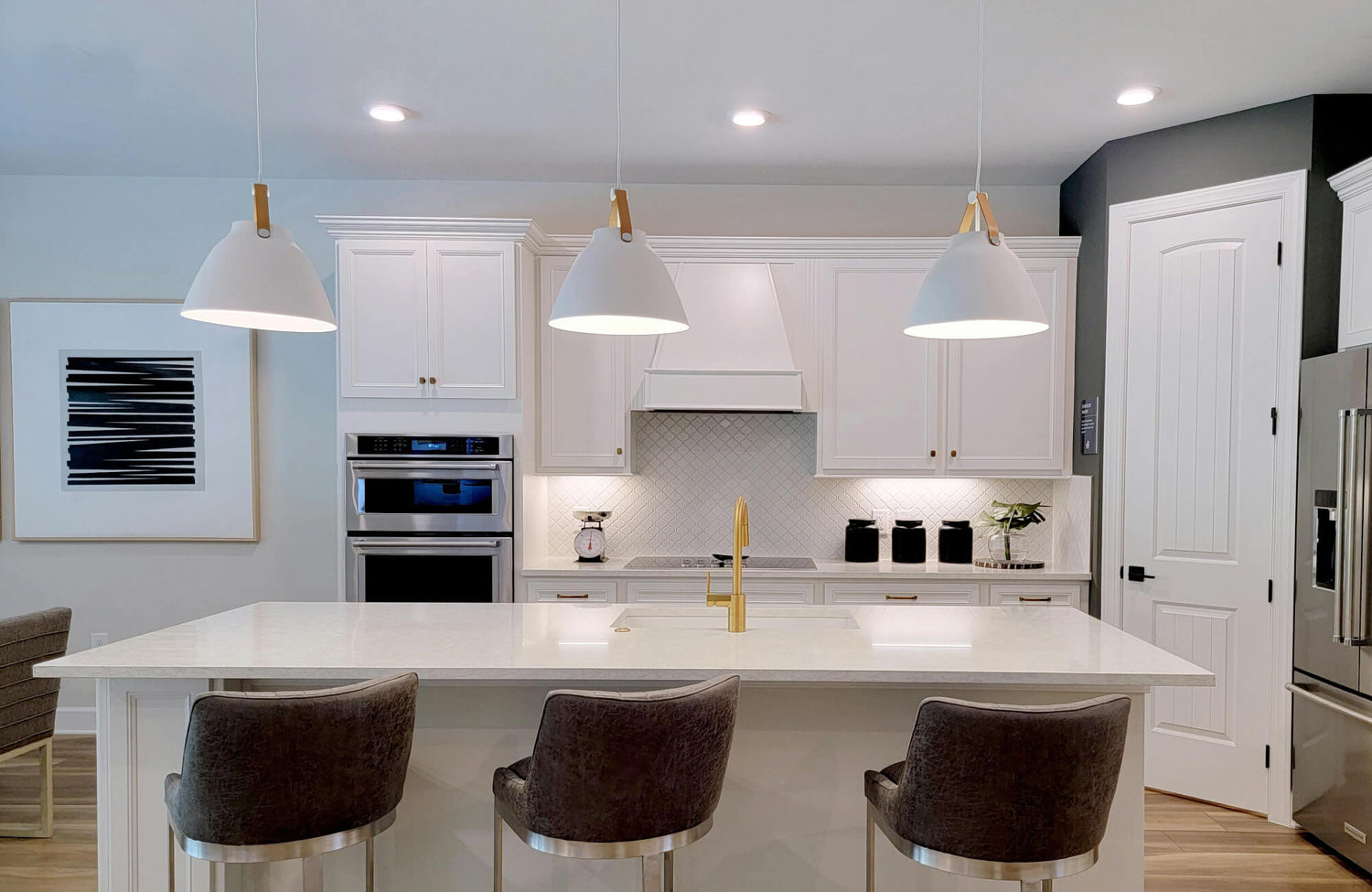 White dome pendant lights with wood accents hang over a waterfall island, set against a white kitchen with arabesque tile backsplash.