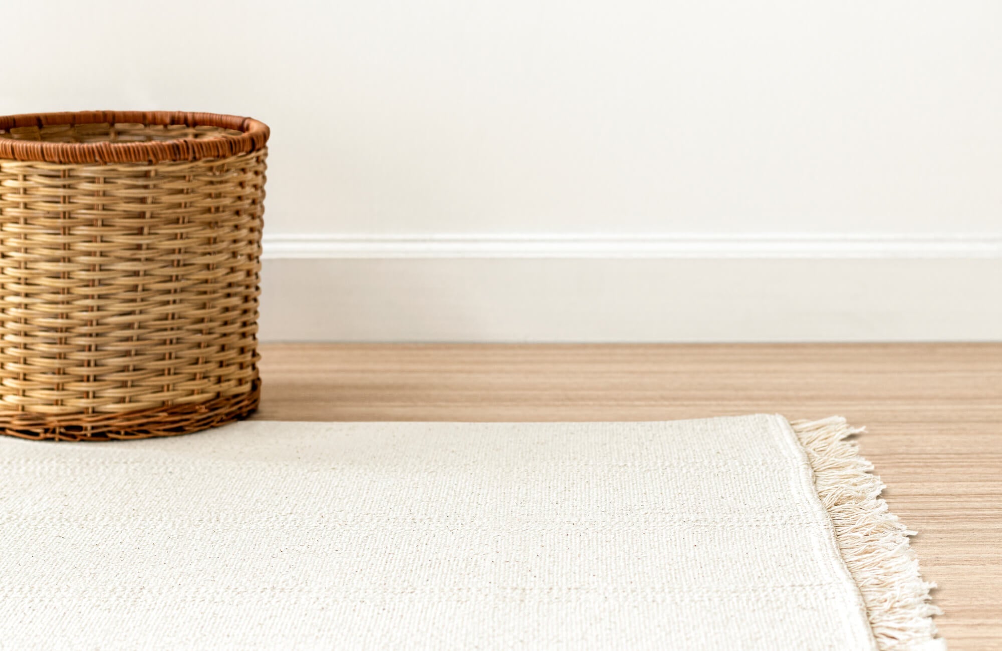 Light-colored rug with woven texture beside a wicker basket on a wood floor, creating a clean, minimal look.